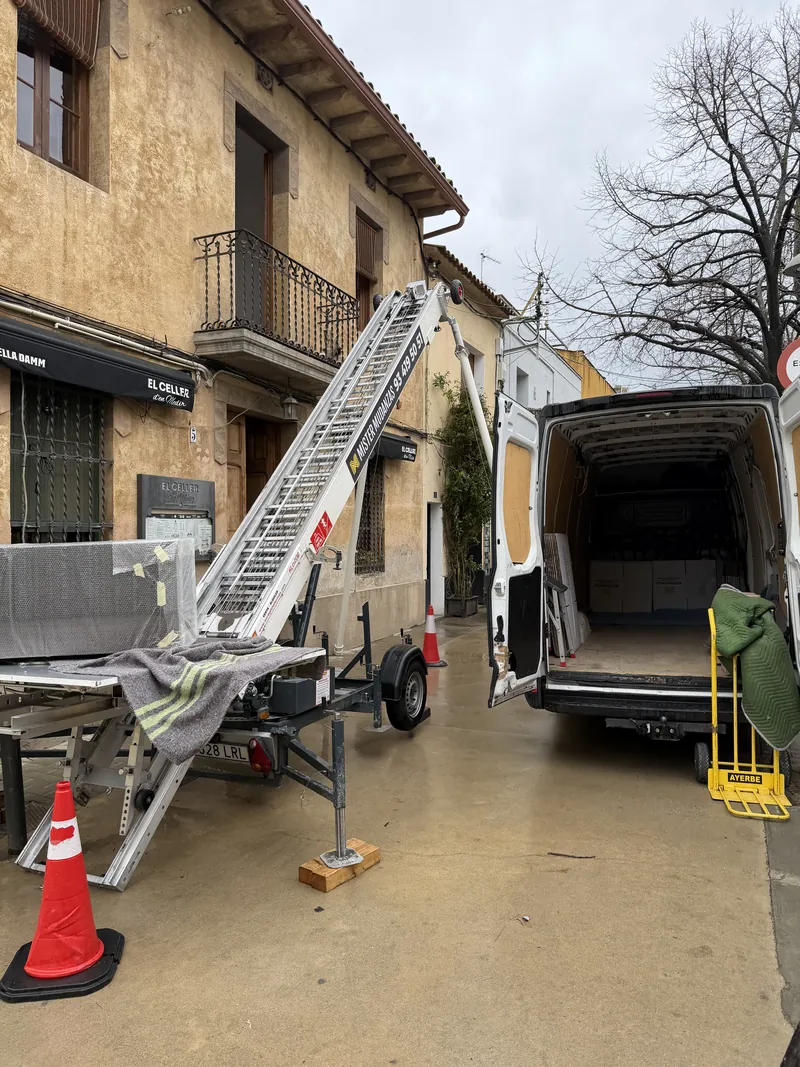 Elevador de mudanzas trabajando en una calle estrecha junto a una furgoneta